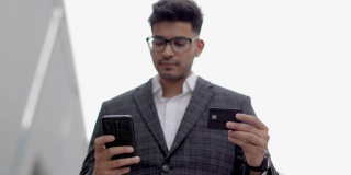 穆斯林男子穿着正式服装，使用信用卡和智能手机购物。