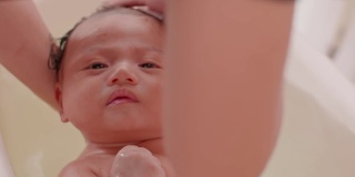 平静的亚洲新生儿沐浴在浴缸。母亲用温水给儿子洗澡。可爱的新生儿微笑在浴缸放松和舒适。新生儿护理理念