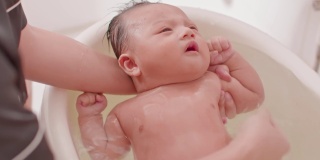 平静的亚洲新生儿沐浴在浴缸。母亲用温水给儿子洗澡。可爱的新生儿微笑在浴缸放松和舒适。新生儿护理理念