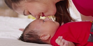 近距离美丽迷人的亚洲妈妈亲吻婴儿脸颊甜和可爱的爱。可爱的亚洲新生儿在床上睡觉和打盹。母亲和新生儿概念。慢动作