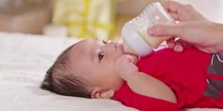 新生儿躺在床上喝着牛奶。可爱的婴儿宝宝用爱在家里喂奶。新生的概念