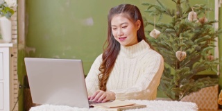 亚洲女商人在圣诞树的背景下在家工作。自由职业女性在圣诞节前夕用电脑在家里工作。假期工作概念
