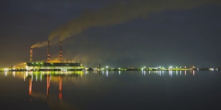 燃煤电厂的高管与黑烟快速移动污染大气在夜间与倒影在湖水。日到夜的时间推移过渡
