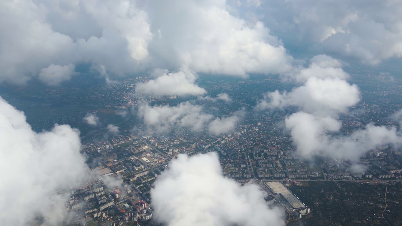 从高空的飞机窗口鸟瞰，远处的城市被暴雨前形成的蓬松的积云所覆盖