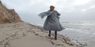 迷人的红发女人在外套跑在野生秋天的海滩
