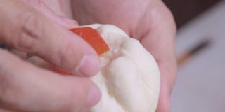 女厨师用手把腌过猪排的面团捏成小圆面包的形状，再在上面放上咸蛋黄。包子的制作过程。