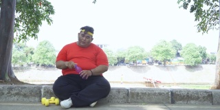 一个肥胖男子坐在公园里喝水