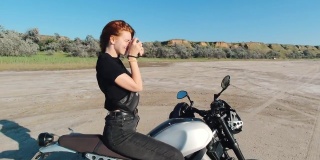 年轻的女摄影师坐在摩托车上，看着日落