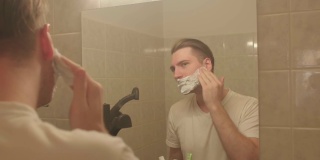 男士将剃须泡沫涂在脸上。他在算盘上搓手，准备刮脸。