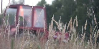 拖拉机正割着屋后地上长着的高草，在夕阳下，透过满是种子的干草可以看到