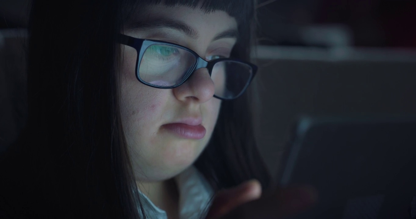 一个患有唐氏综合症的十几岁女孩晚上坐在家里的沙发上用平板电脑娱乐。技术概念，连接，残障，残障，在线，沟通