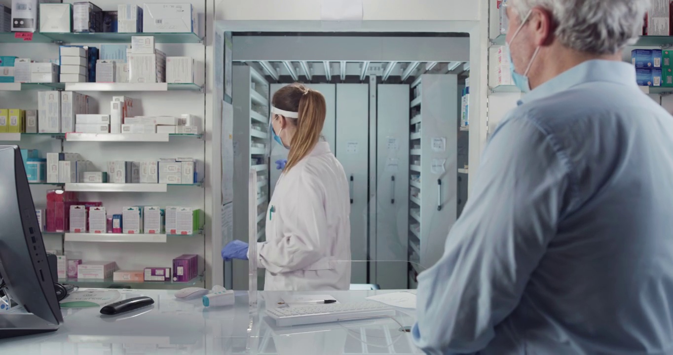 电影镜头的药剂师带着医用口罩在药房对男性患者做冠状病毒鼻咽拭子试验。概念:covid-19、保护、安全、大流行、预防、援助