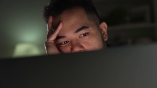 亚洲男人在家里使用电脑工作到很晚时，感觉不开心，有压力和疲倦。视频素材模板下载