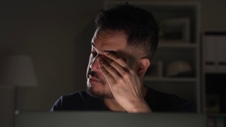 亚洲男人在家里使用电脑工作到很晚时，感觉不开心，有压力和疲倦。慢动作视频素材模板下载