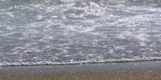 波浪在沙滩上汹涌而过，白色的泡沫填满了屏幕，然后以慢镜头的方式退去又退去