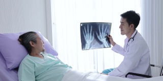 亚洲男医生手握骨x光片与患者交谈，讲解治疗方法，鼓励亚洲男老年患者术后进行治疗