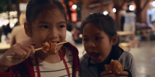 亚洲姐弟小女孩在泰国夜市街头小吃吃热狗美味的街头小吃。