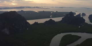 在泰国攀牙湾的红树林和茂密的雨林上空，可以看到多山的岛屿和海洋上引人注目的橙色日出