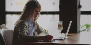 一名中国女子坐在窗边，拿着笔记本电脑，在笔记本电脑盒里写东西，看着屏幕做任务