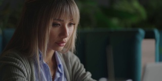 一位亚洲女性坐在那里，看着笔记本电脑屏幕，沉思着。他的脸上满是头脑风暴和焦虑。沉思的亚洲女人