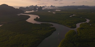 在泰国攀牙湾的红树林和茂密的雨林上空，可以看到多山的岛屿和海洋上引人注目的橙色日出