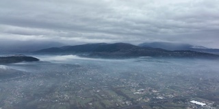 从空中俯瞰，在一个多云的日子里，从空中俯瞰一个美丽的山谷和远处的山脉。