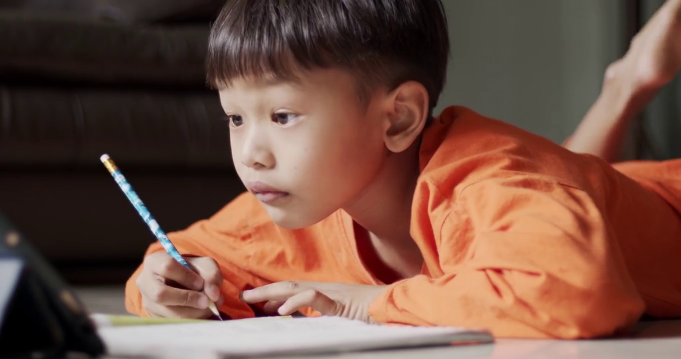 穿着橙色衬衫的男孩正专注于在线学习。