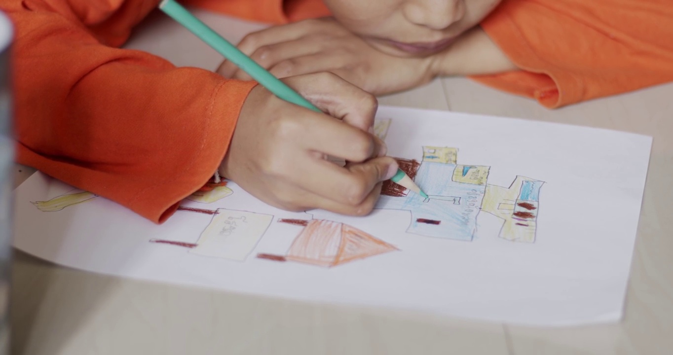 穿着橙色衬衫的小男孩正在纸上画画。