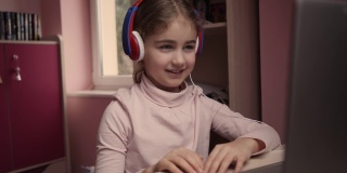 远程学习。用笔记本电脑在线学习的女生在抄写本上做笔记。学生戴耳机观看网络视频课程。白种人女孩戴耳机学习在线课程