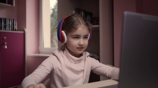 远程学习。一名女学生用笔记本电脑在线学习。学生戴耳机观看网络课程。未来的程序员学习编程。孩子玩电脑游戏。视频素材模板下载