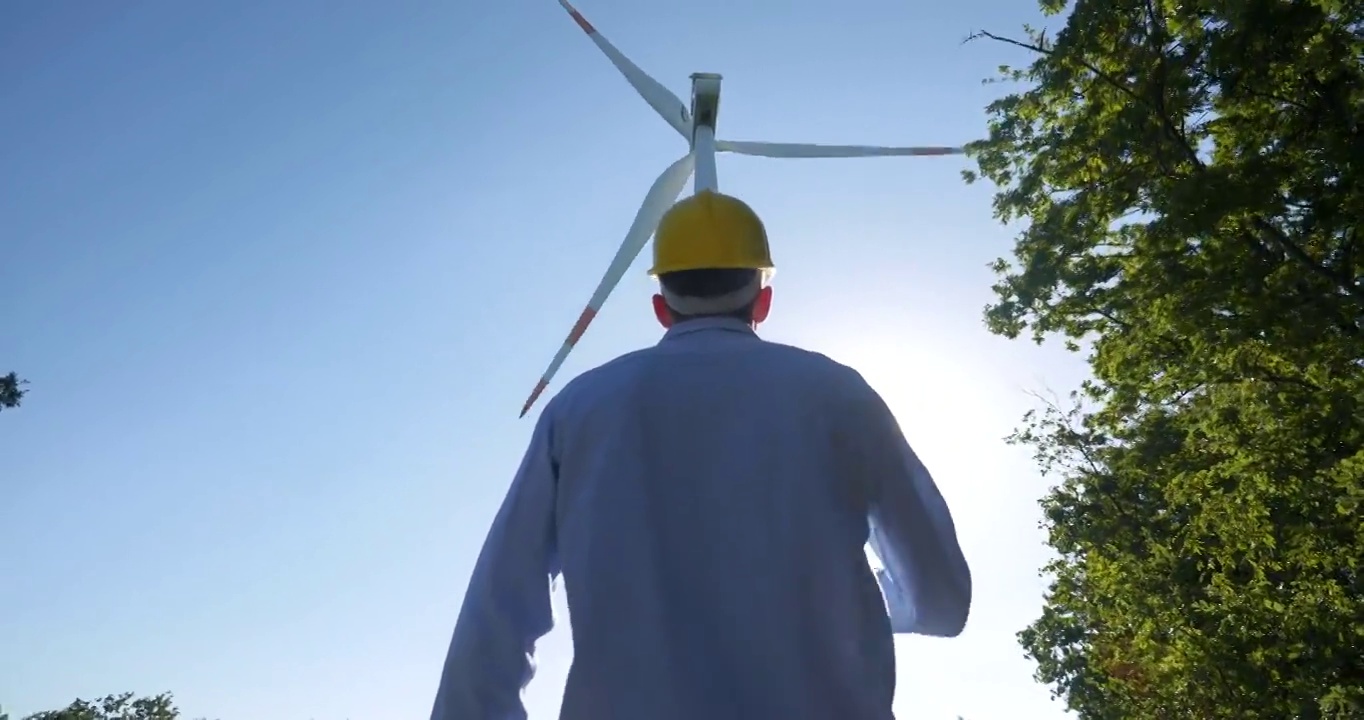 日落时分，一位年轻的工程师正在检查风车的正确操作和效率。理念:可再生能源、技术、电力、服务、绿色、未来