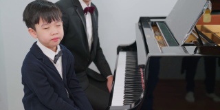 钢琴家在学校教一个男孩弹钢琴。最喜欢的古典音乐。孩子在钢琴教室里打呵欠。身着正式优雅套装的音乐家。教育、练习、放松的理念。