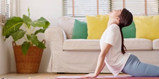 健康迷人的亚洲女性在休闲做瑜伽Cobra姿势在家里冥想舒适和放松，冷静的健康年轻女性深呼吸和冥想与瑜伽在家里，瑜伽概念