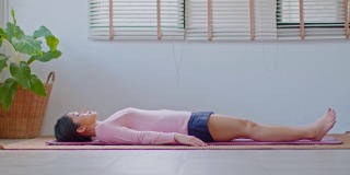 平静的亚洲妇女练习瑜伽死尸或Savasana姿势与冥想微笑在家里感觉如此舒适和放松，保健概念