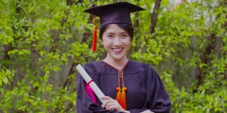 迷人的亚洲女学生毕业，戴着帽子，穿着长袍，手拿证书，在毕业典礼上自豪地庆祝，祝贺学生毕业，教育成功