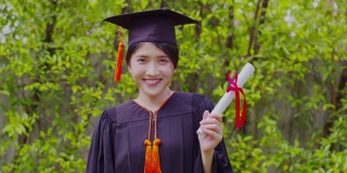 迷人的亚洲女学生毕业，戴着帽子，穿着长袍，手拿证书，在毕业典礼上自豪地庆祝，祝贺学生毕业，教育成功