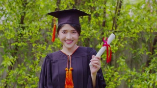 迷人的亚洲女学生毕业，戴着帽子，穿着长袍，手拿证书，在毕业典礼上自豪地庆祝，祝贺学生毕业，教育成功视频素材模板下载