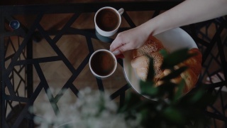 女人正在把咖啡杯放在桌子上。新鲜Сroissants。早上好，醒醒。心情舒畅，周末在家放松。美味的甜蜜的早餐。视频素材模板下载