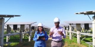 身穿蓝色防护服、安全眼镜、安全帽的亚洲中年工程师与非洲投资者在太阳能农场散步时在平板电脑上做笔记
