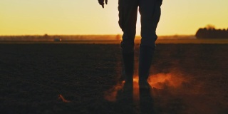 日落时分，一个穿着胶靴的农民穿过犁过的田野