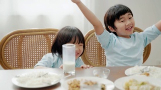 亚洲家庭关系，兄弟姐妹在早餐桌上争夺牛奶。视频素材模板下载