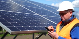 戴着头盔的男子在太阳能电池板的背景上使用智能手机。太阳能发电厂工人男性肖像