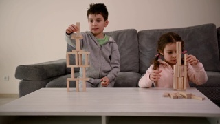 可爱的欧洲孩子一起玩棋盘游戏。一个英俊的学龄男孩，用木砖砌成房子，坐在沙发上，旁边是他的小妹妹，她的塔倒塌了，她很难过视频素材模板下载