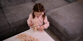 俯视图集中可爱的小白人女孩玩木砖，同时用积木建造木结构。棋盘游戏和精细运动开发、教育理念