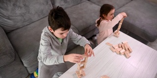 头顶上，英俊的学龄白人男孩和他的妹妹正在用砖块搭建木结构。棋盘游戏和精细运动开发、教育理念