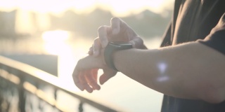 亚洲男性早晨日出时在公园跑步使用智能手表按下start键记录并观察心率，保持健康。