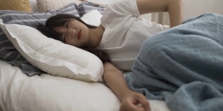 亚洲妇女在家里的卧室里忍受着月经疼痛，蜷缩在床上，抱着自己的肚子。