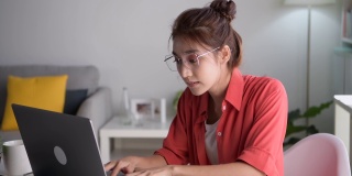 年轻的亚洲妇女坐在眼睛闭从疲惫和疲倦在工作在家庭办公室使用笔记本电脑。劳累过度的亚洲女学生工作人员，在电脑工作后因疲劳而按摩眼睛和太阳穴