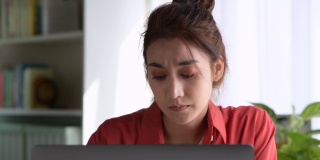 年轻的亚洲妇女坐在眼睛闭从疲惫和疲倦在工作在家庭办公室使用笔记本电脑。劳累过度的亚洲女学生工作人员，在电脑工作后因疲劳而按摩眼睛和太阳穴