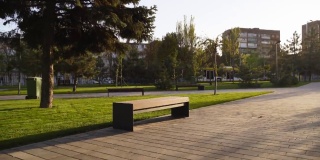 公园草坪上的现代木凳。时尚的新长椅在城市休闲区日出或日落。城市主义主题公共空间景观设计。空旷的街道人行道上没有人